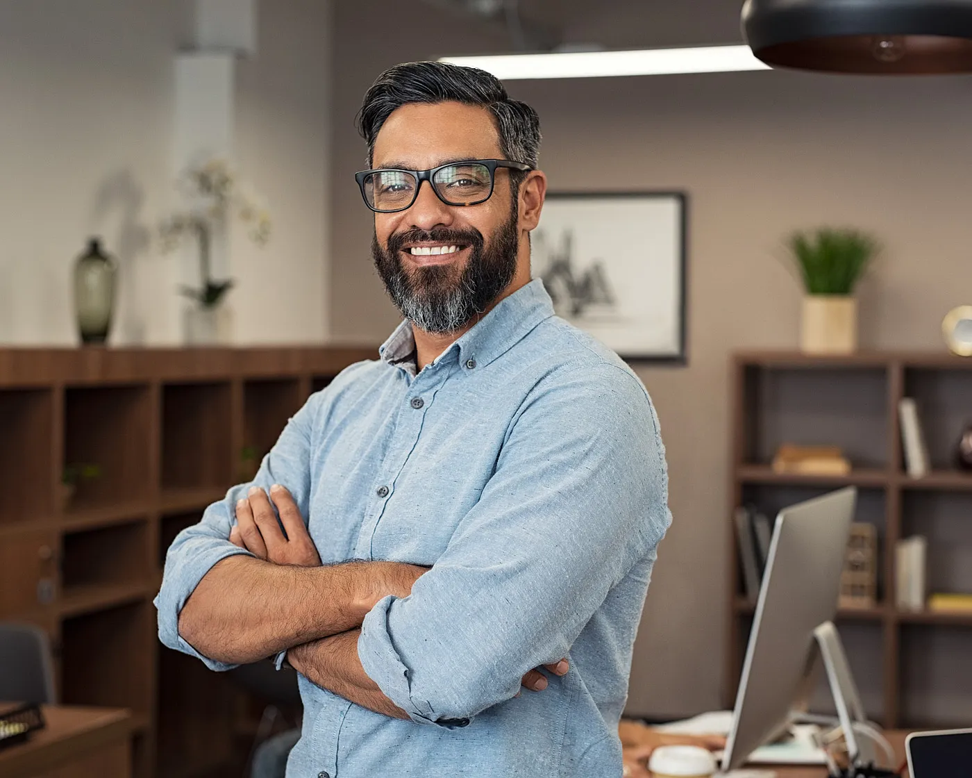 Smiling man with glasses standing with his arms folded in an office