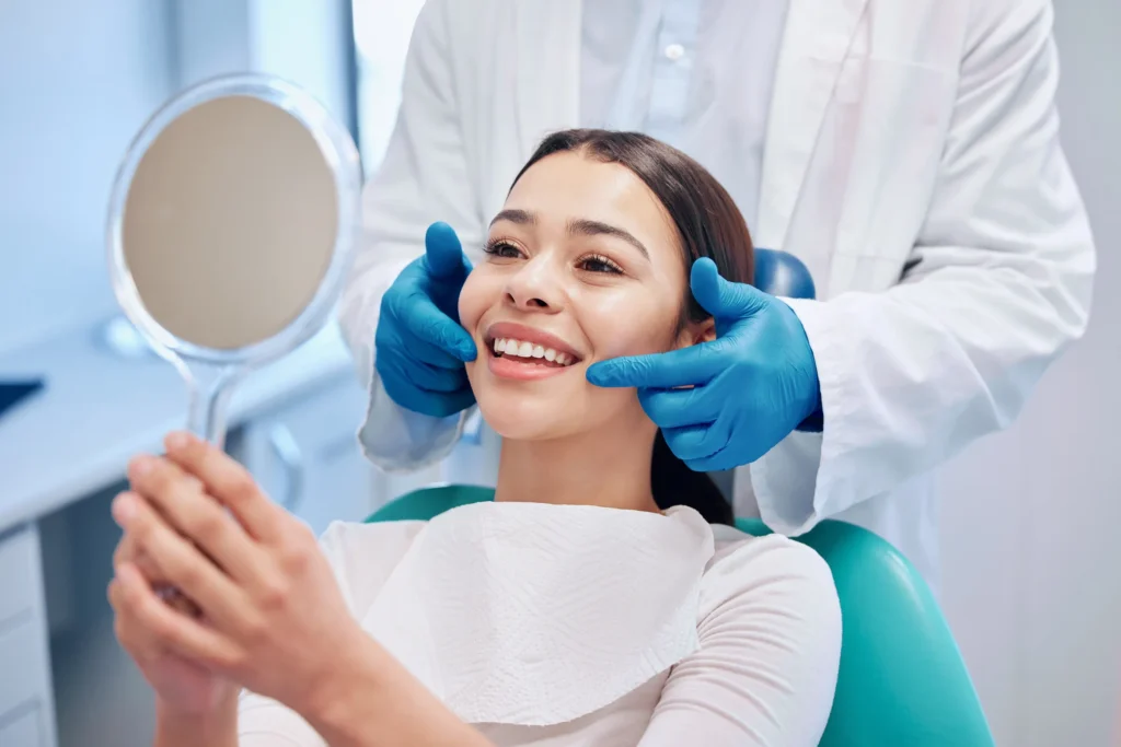 Woman in a dental chair holding a mirror while the dentist frames her smile