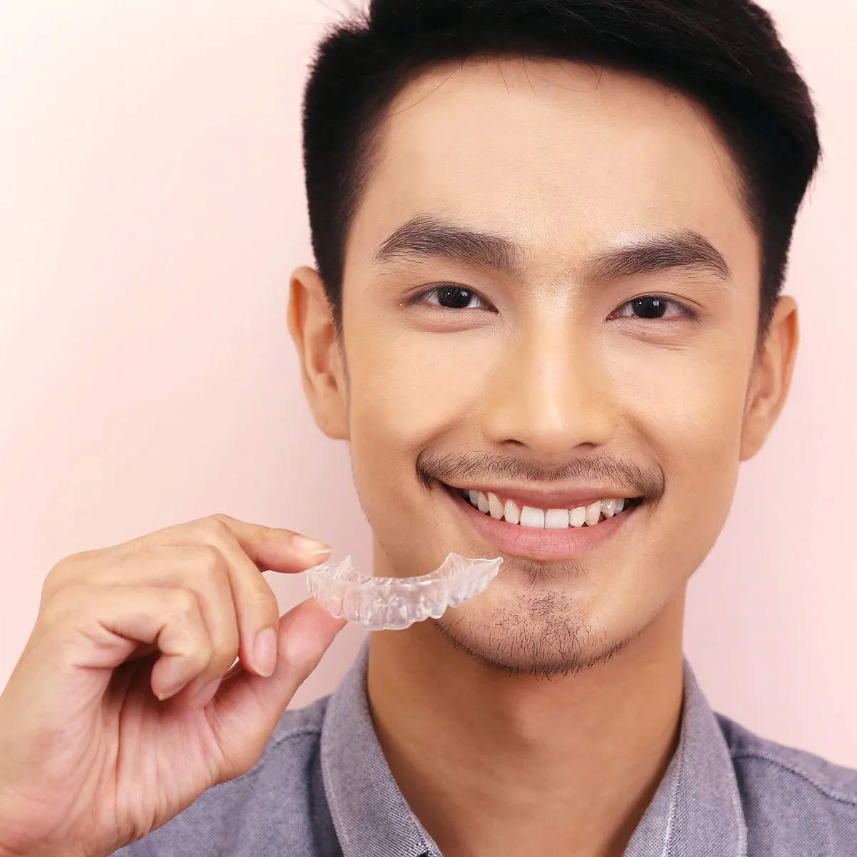 Smiling man holding a clear aligner tray beside his face