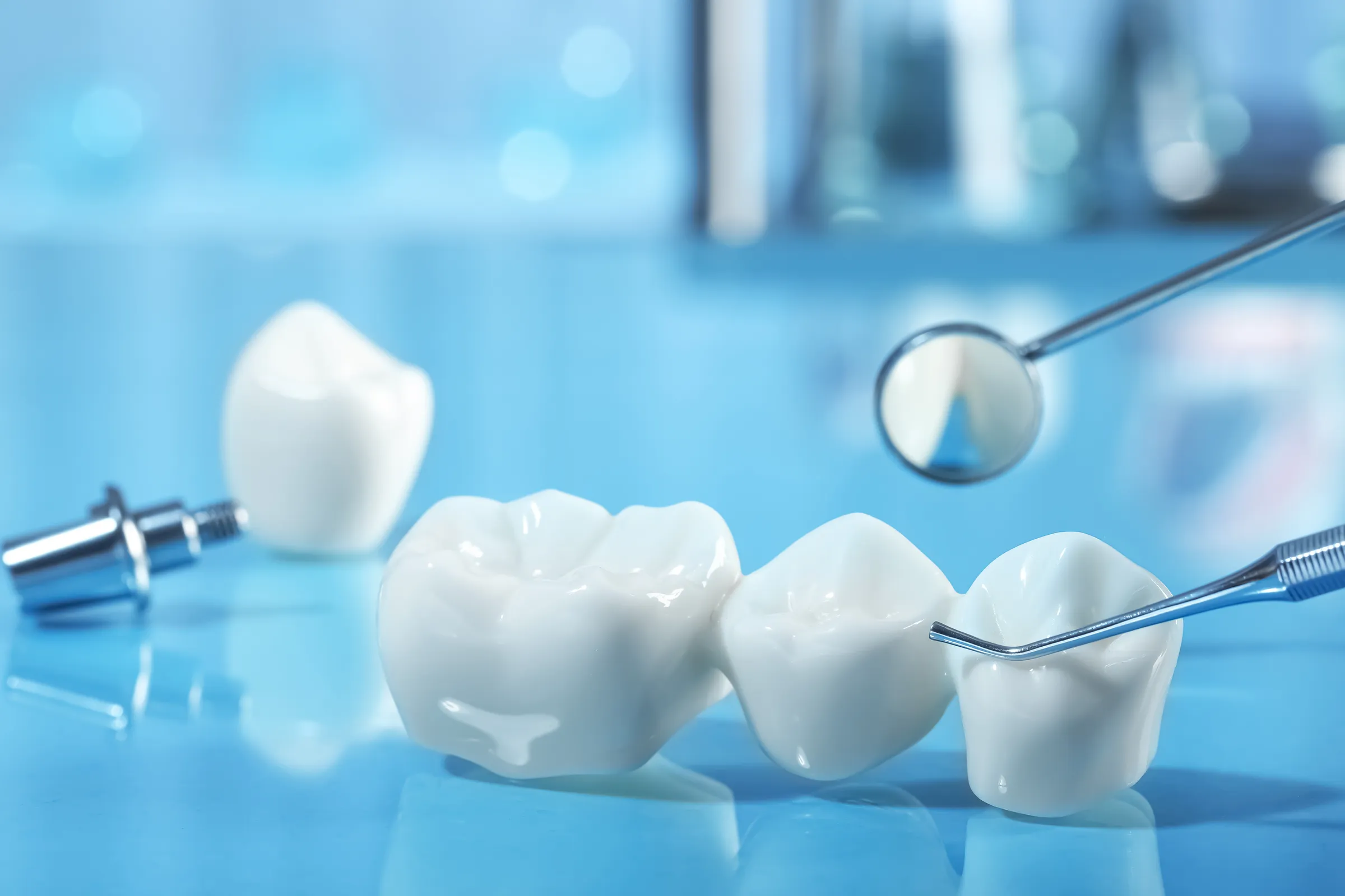 Dental crowns and an implant post on a work surface beside a dental mirror