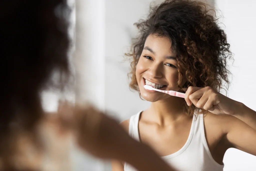 A woman smiling as she brushes her teeth at a bathroom mirror