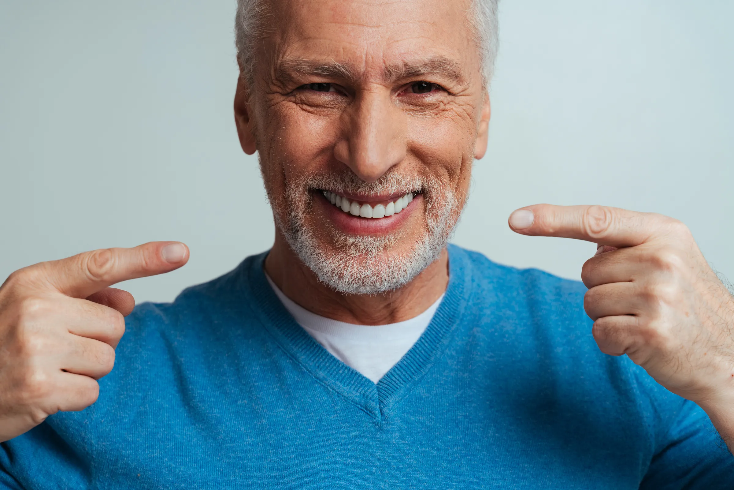 Smiling older man in a blue jumper pointing at his teeth