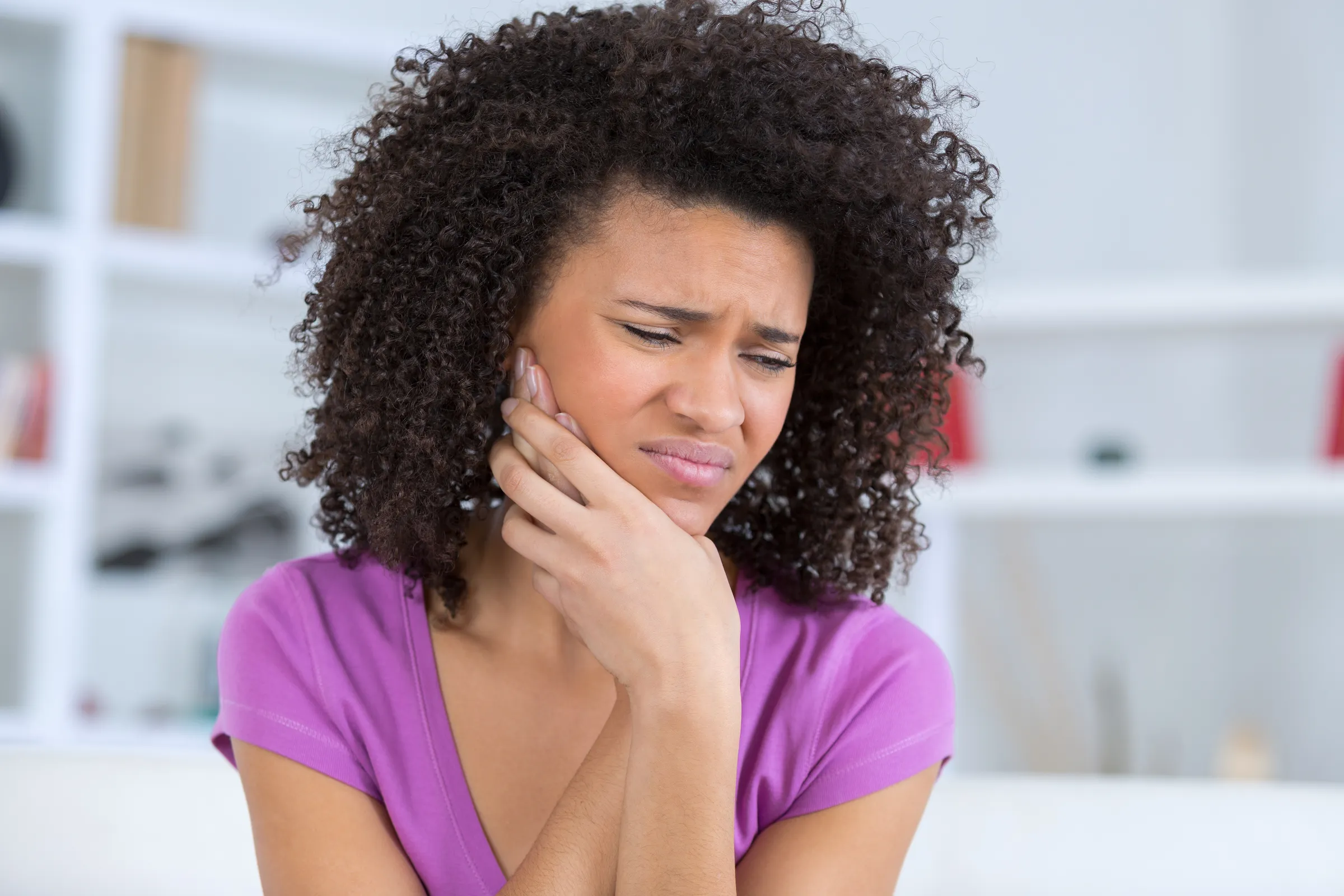 A woman wincing and holding her jaw in dental pain
