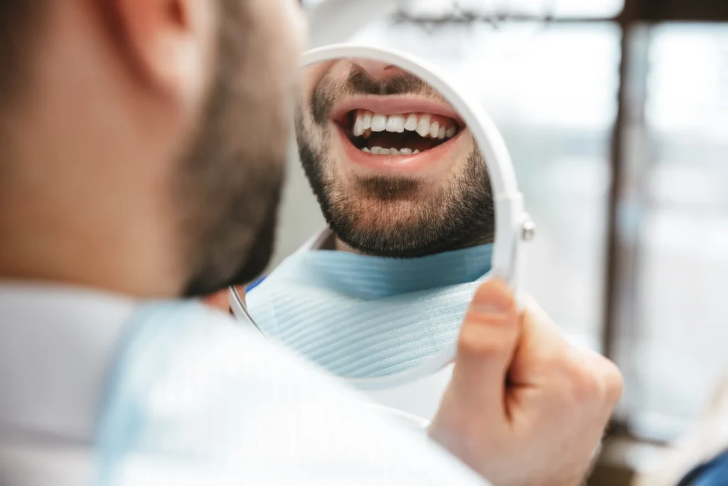 Man in a dental chair holding a mirror and smiling