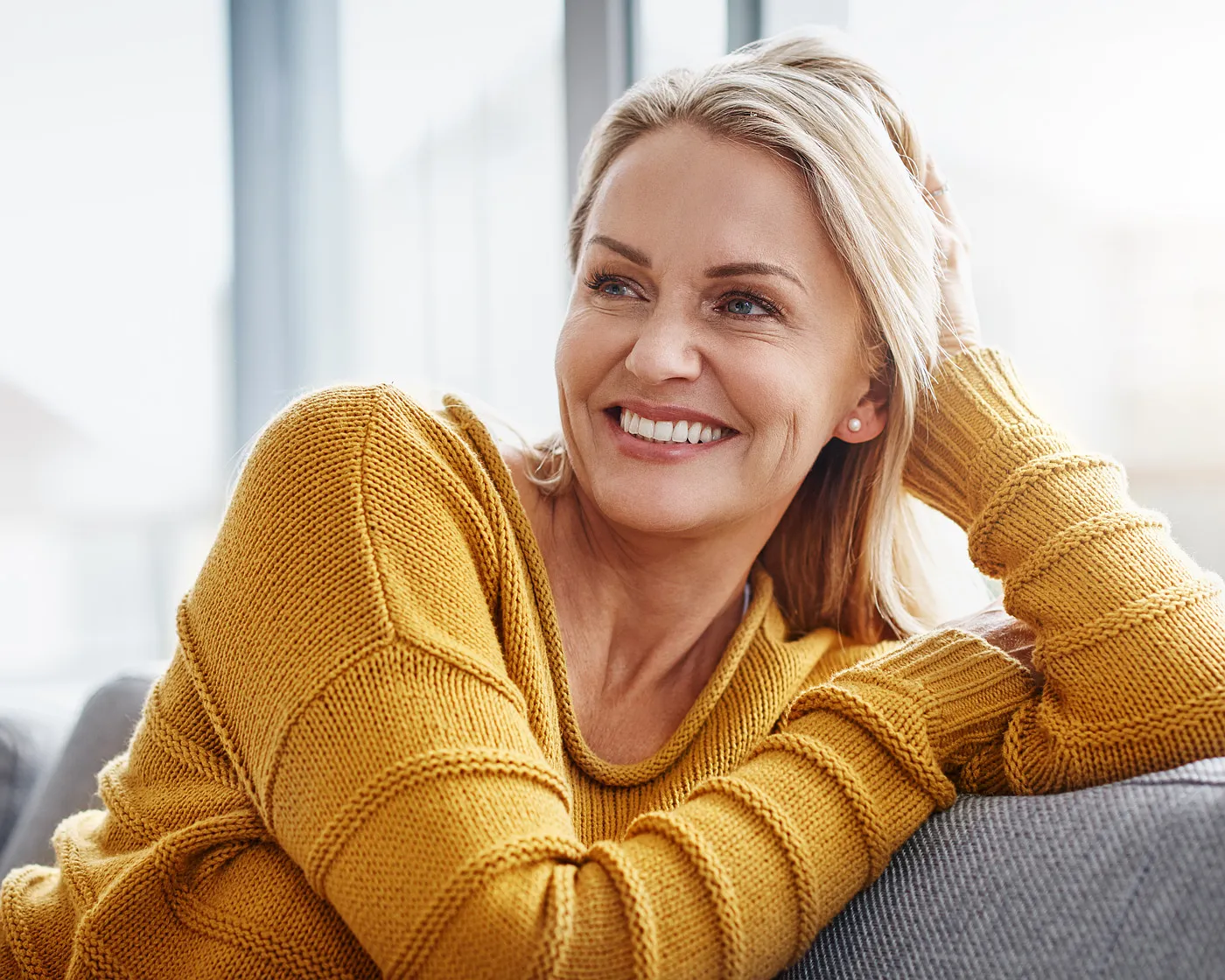 Smiling older woman in a yellow jumper on a sofa