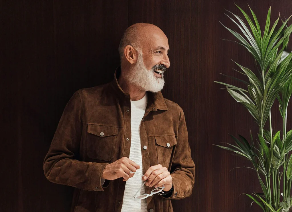 Smiling older man with a white beard standing beside a plant