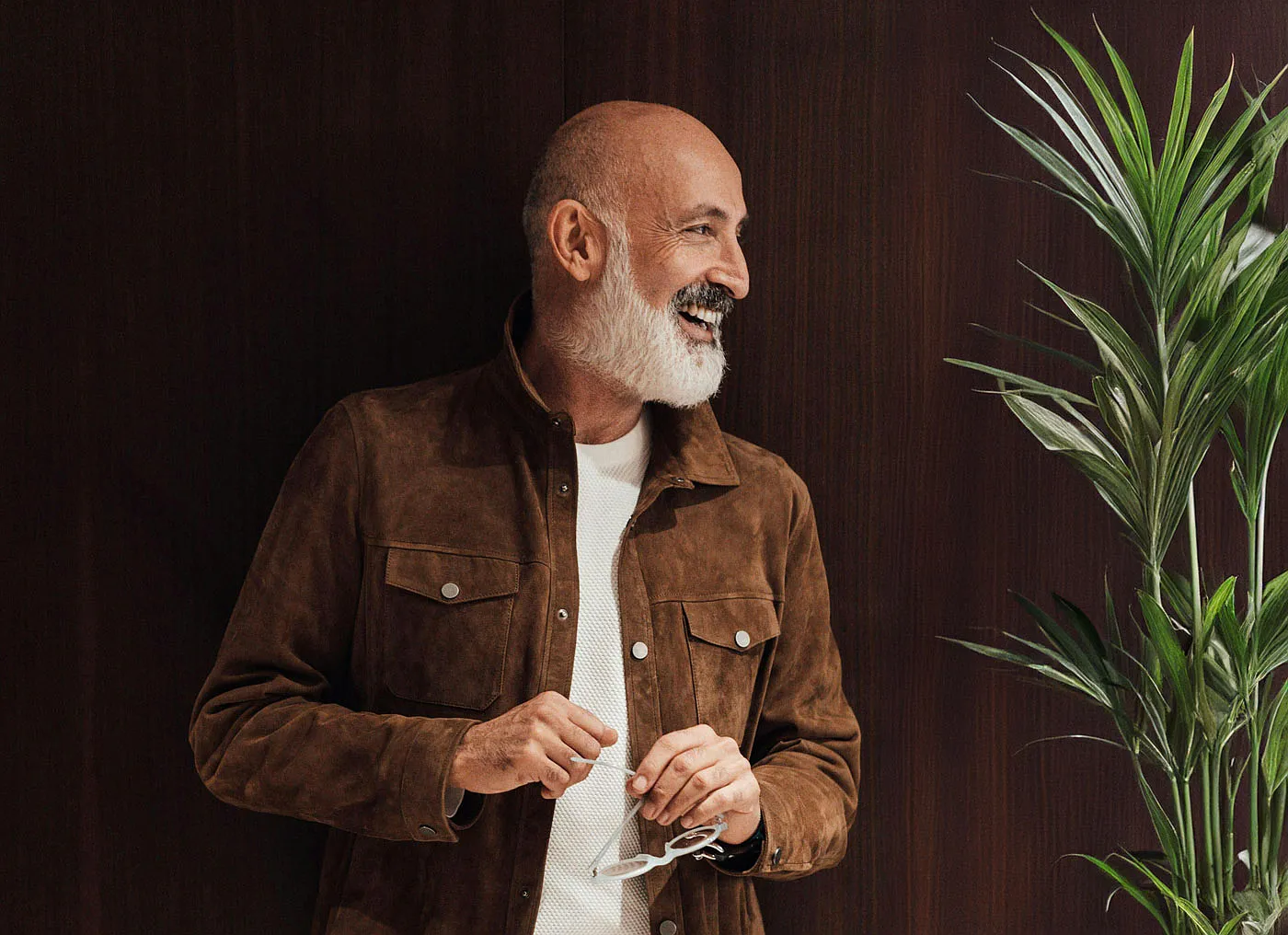 Smiling older man with a white beard standing beside a plant