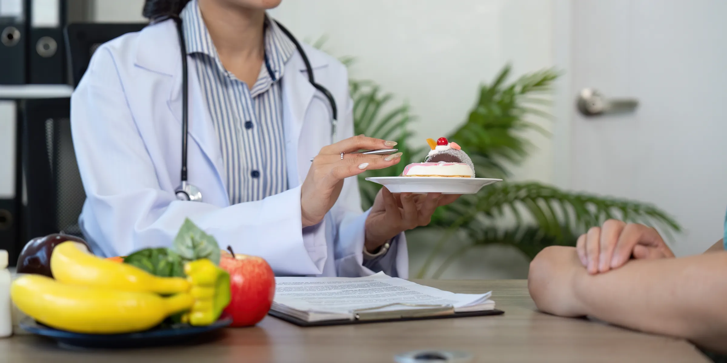 Clinician holding a dessert beside fruit and vegetables during a nutrition consultation
