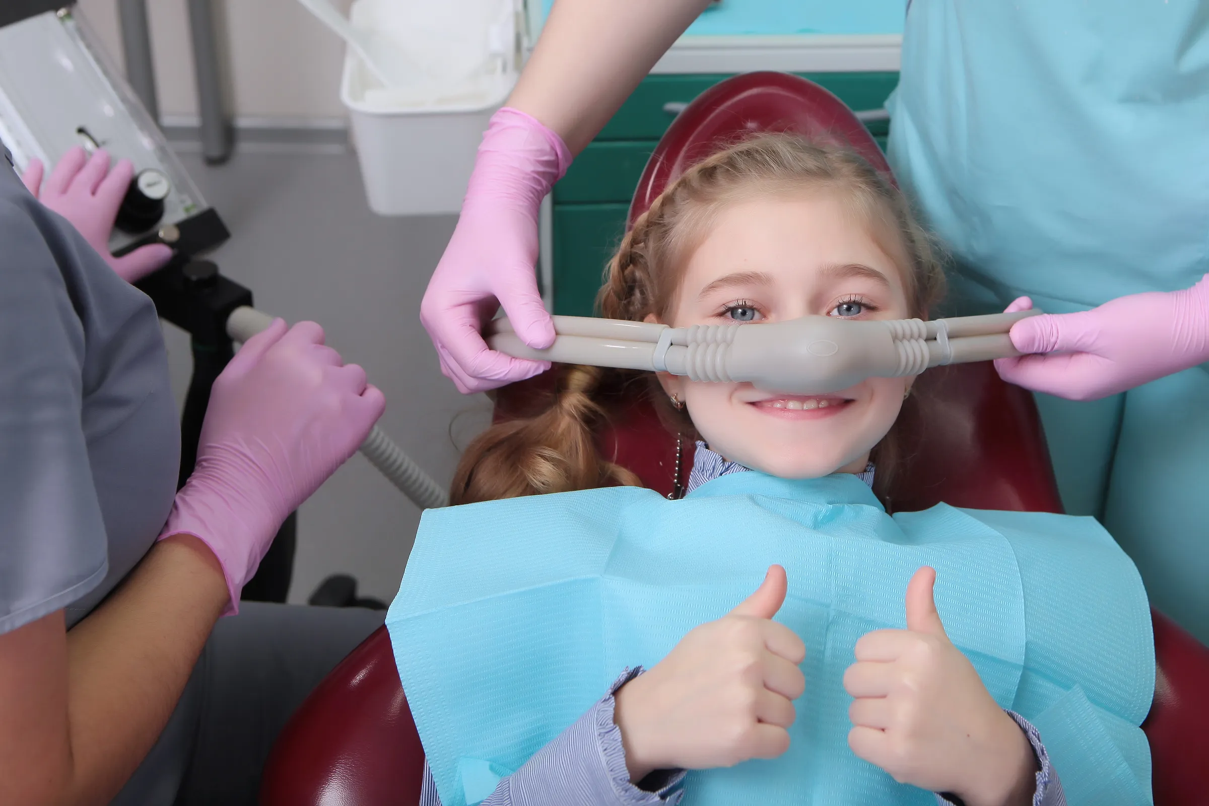 Child in a dental chair giving a thumbs up while wearing a nitrous oxide mask