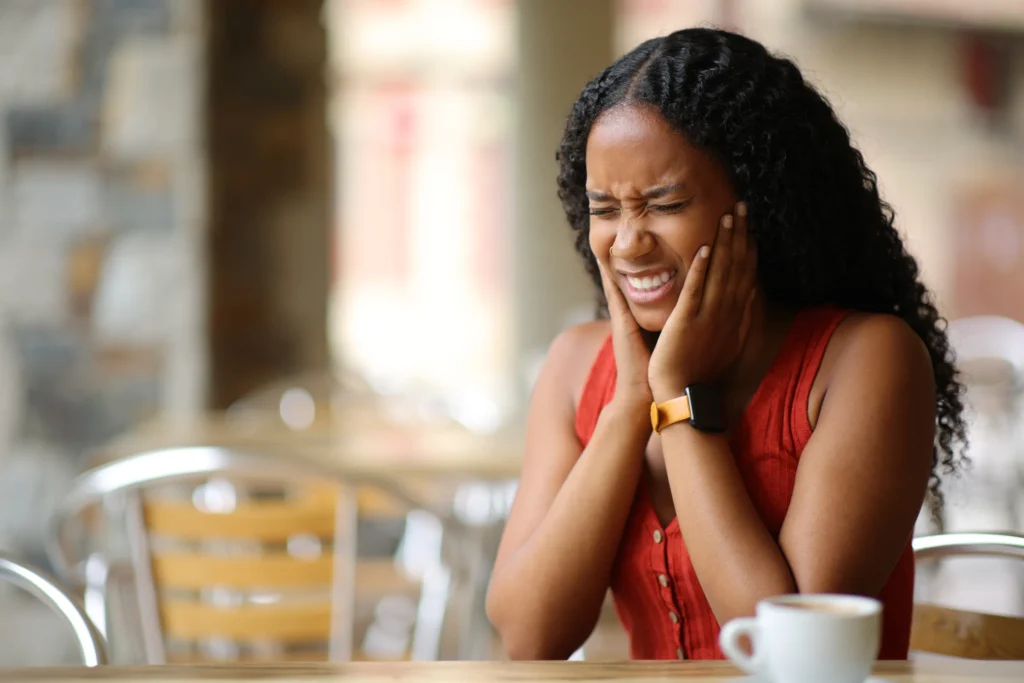 Woman holding her cheek in pain at a cafe table