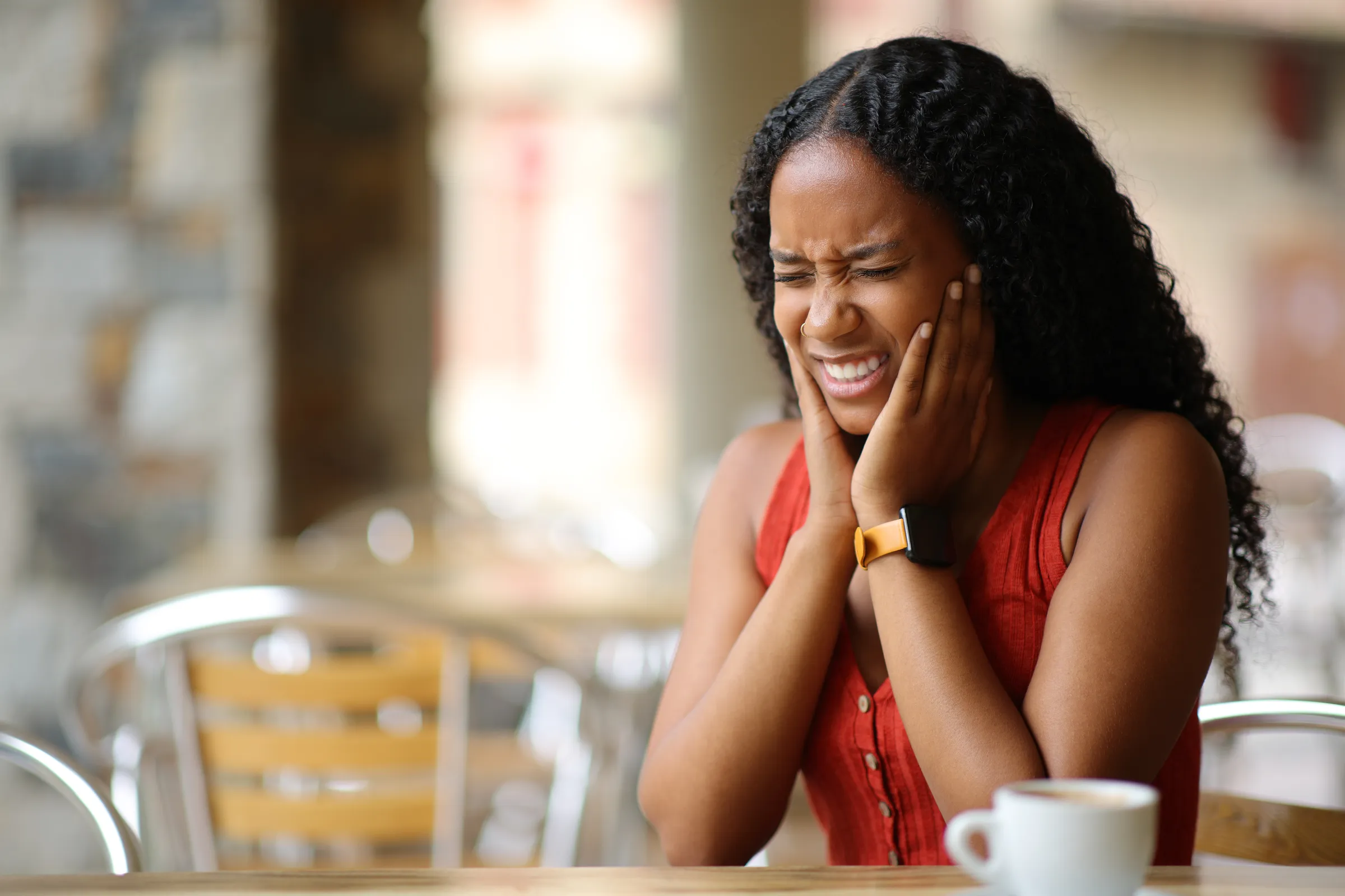 Woman holding her cheek in pain at a cafe table