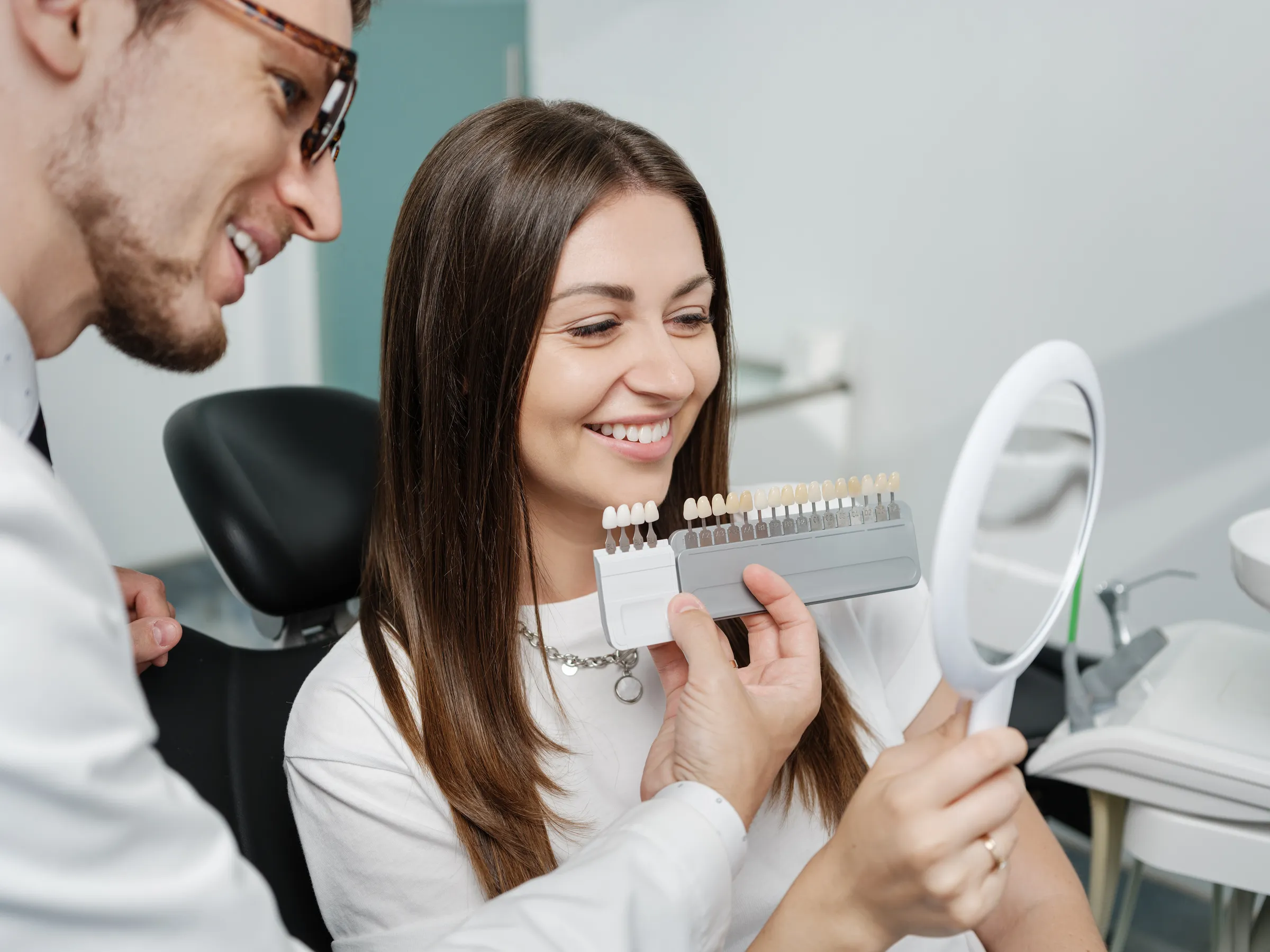 Woman in a dental chair choosing a tooth shade with a mirror