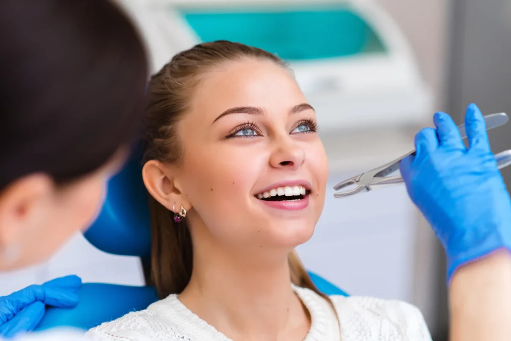 A young woman smiling in a dental chair while a dentist works with an instrument