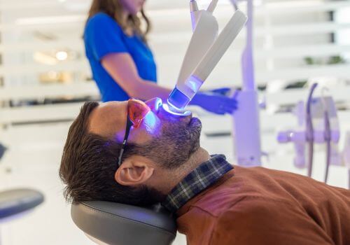 A patient undergoing in-office teeth whitening under a blue curing lamp