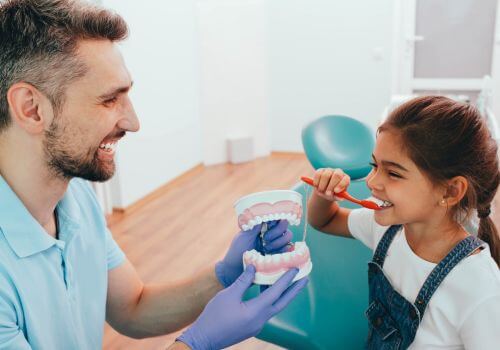Young girl learning how to brush her teeth from her dentist