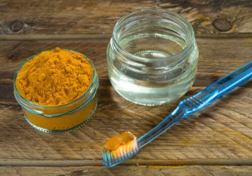 Turmeric powder and a jar of liquid beside a toothbrush, a natural teeth-whitening remedy