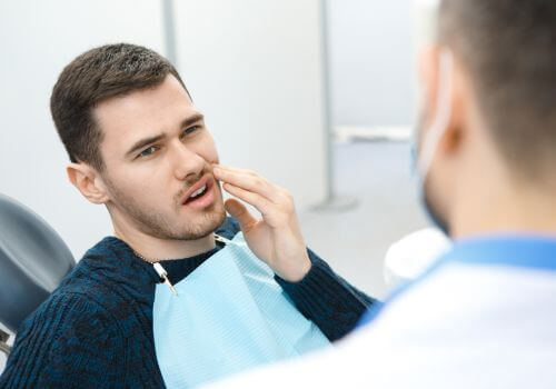 Man in a dental chair wincing from pain from a tooth infection