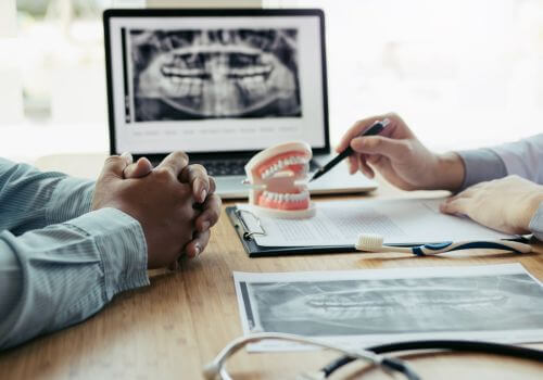 A dentist reviewing a panoramic X-ray and a dental model with a patient