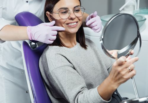A patient in the dentist's chair looking at her smile in a handheld mirror