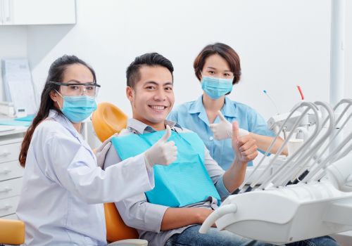 A patient and two dental team members giving a thumbs up in the treatment room