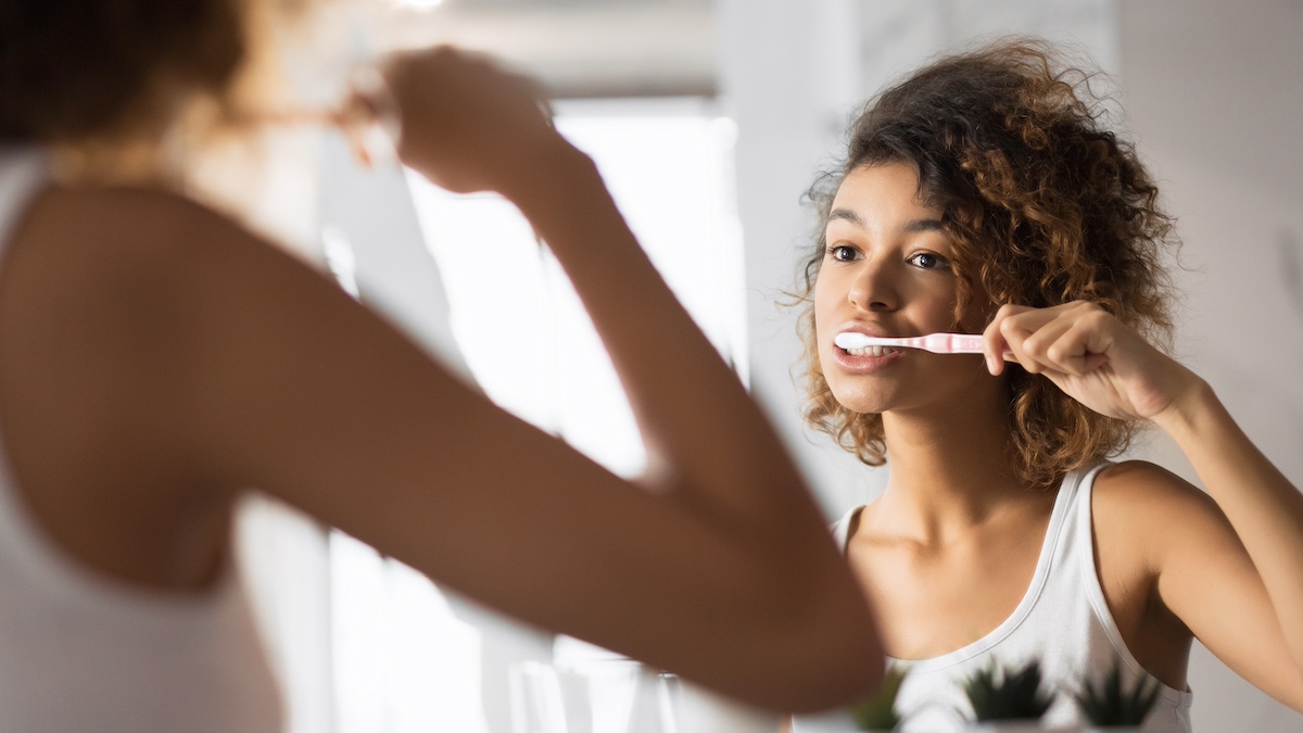 A woman brushing her teeth at a bathroom mirror, seen in the reflection