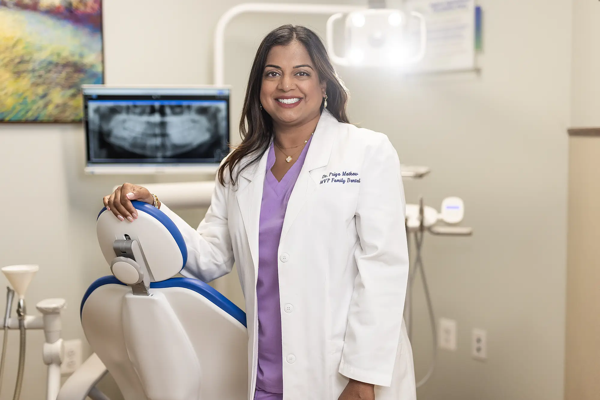 Dr. Priya Mathew standing beside a dental chair in a treatment room