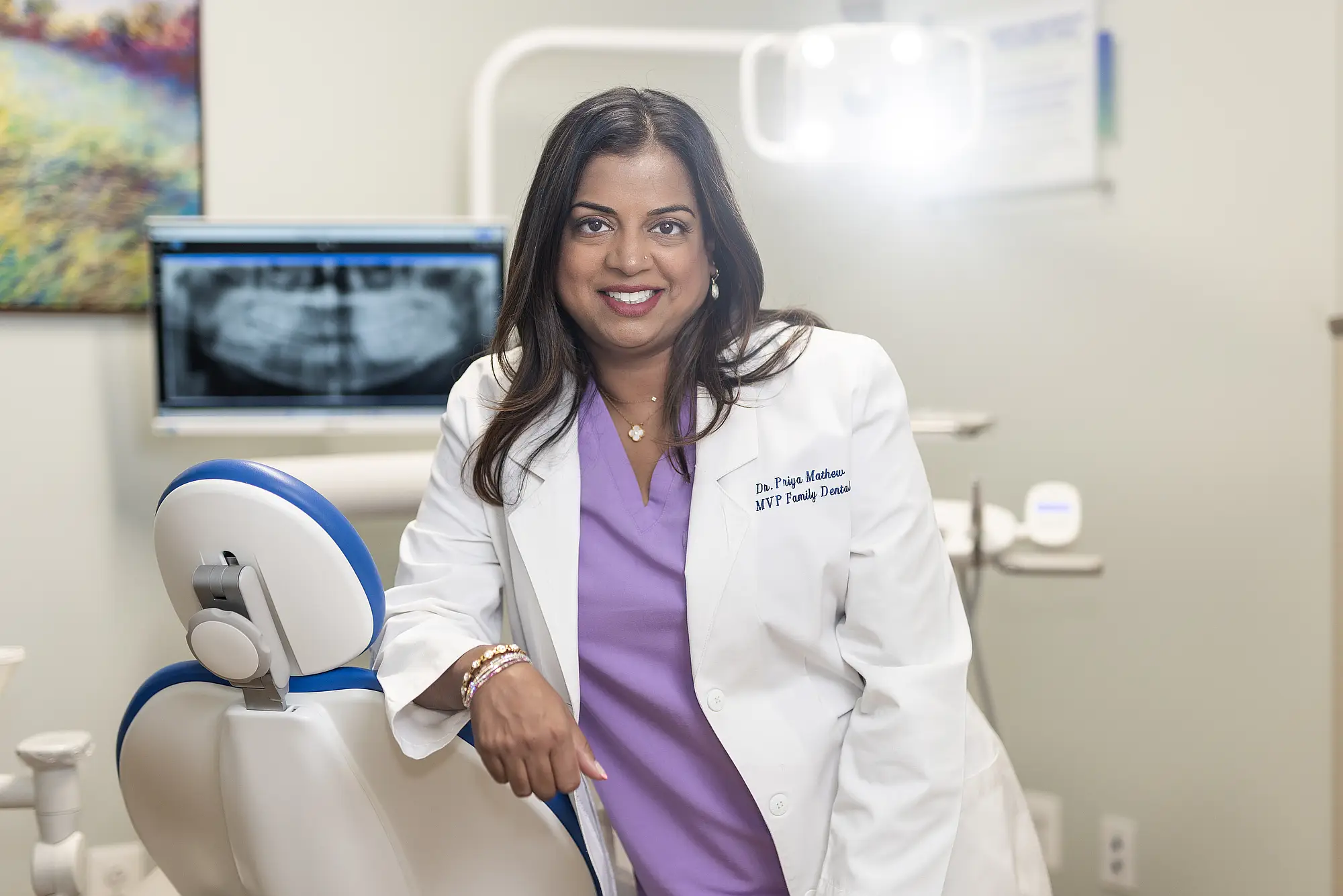 Dr. Priya Mathew smiling beside a dental chair
