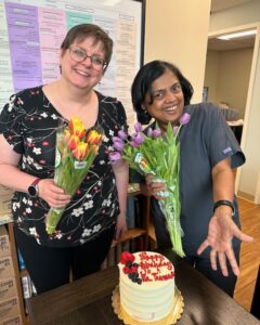 Two team members celebrating a birthday with flowers and a cake