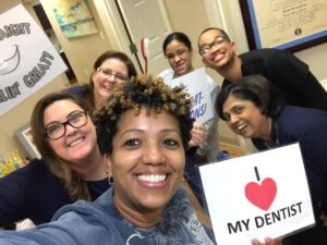 Team members smiling together holding an I love my dentist sign