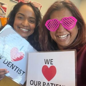 Two team members in novelty glasses holding a We love our patients sign
