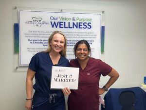 Two team members, one holding a Just Married sign, by the vision and purpose board