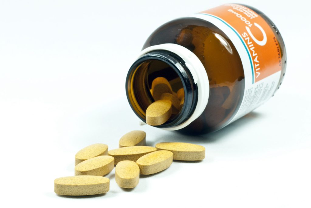 A supplement bottle tipped on its side with vitamin tablets spilling out