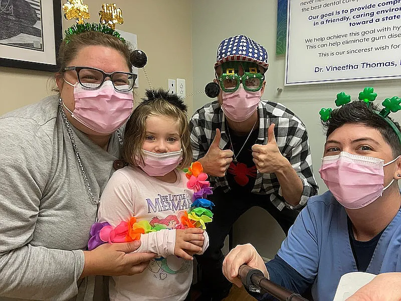 Team members and a child in costume and flower leis smiling for a group photo