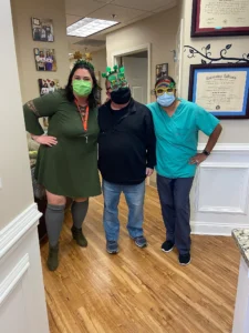 Patients and dental team member wearing festive St. Patrick's Day glasses in the MVP Family Dental hallway