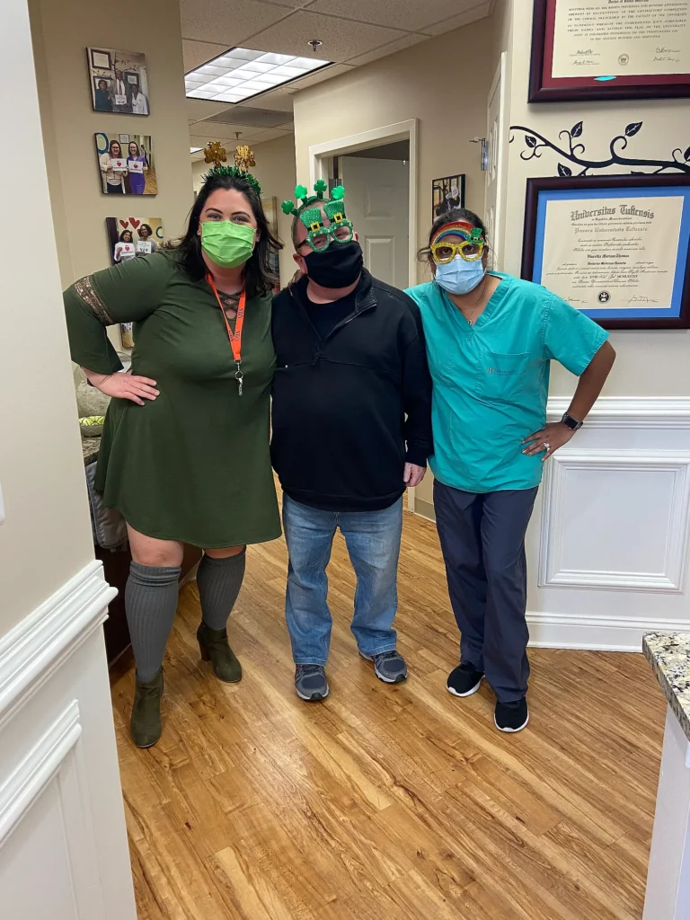 Patients and dental team member wearing festive St. Patrick's Day glasses in the MVP Family Dental hallway