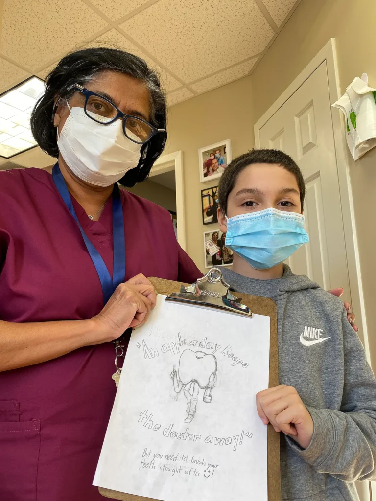 Dental team member with a young patient holding a hand-drawn tooth picture on a clipboard