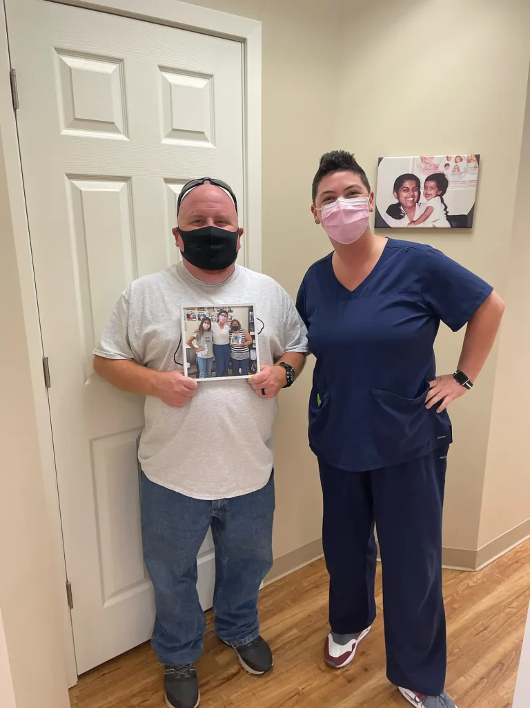 Patient holding a framed photo next to a dental team member in scrubs