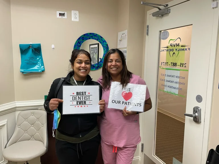 Patient holding a Best Dentist Ever sign beside a team member holding a We Love Our Patients sign