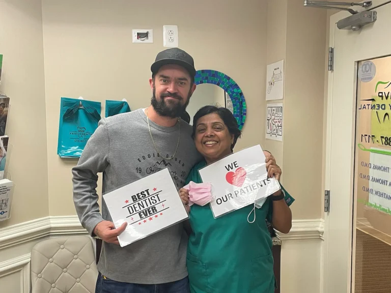 Patient holding a Best Dentist Ever sign with a dental team member holding a We Love Our Patients sign