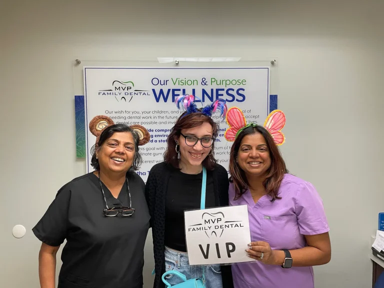 Patient holding a VIP sign with two team members in front of the MVP Family Dental Wellness vision board