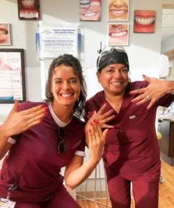 Two MVP Family Dental team members in maroon scrubs showing off their manicures and smiling