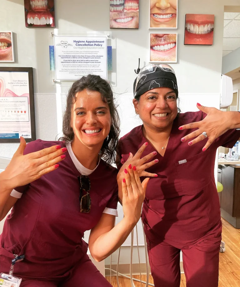 Two MVP Family Dental team members in maroon scrubs showing off their manicures and smiling