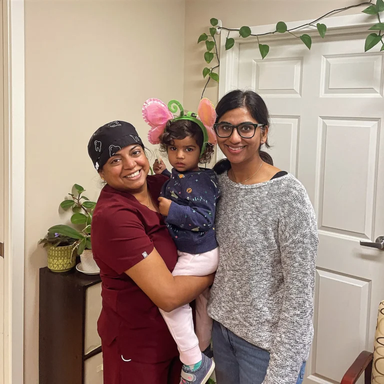 Dental team member holding a toddler in a butterfly headband next to a parent