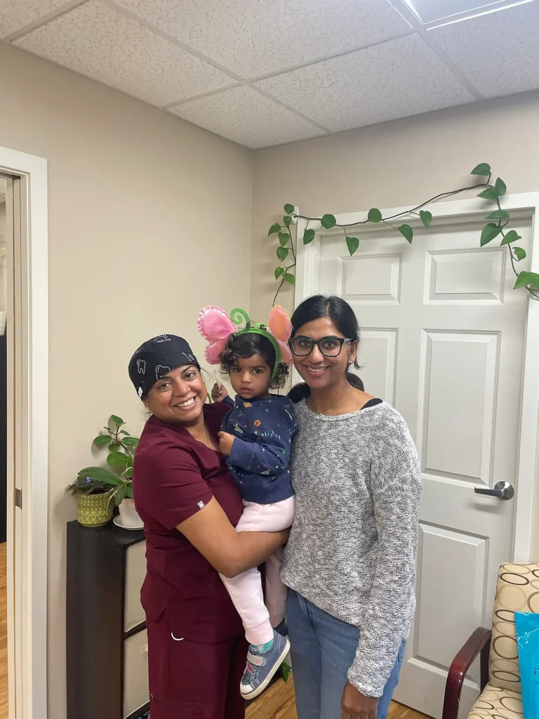 Dental team member holding a young child with a parent beside a doorway at MVP Family Dental