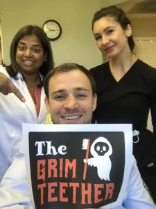 Dentist and team member with a patient holding a Grim Teether Halloween sign
