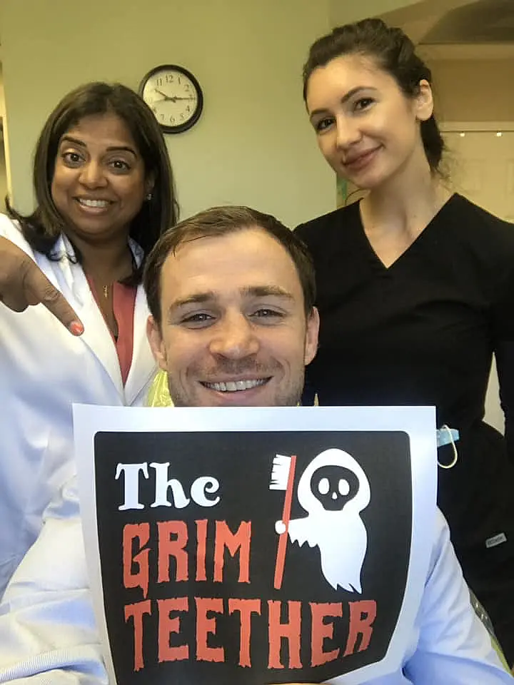 Dentist and team member with a patient holding a Grim Teether Halloween sign