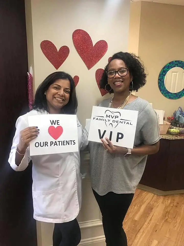 Dentist holding a We Love Our Patients sign next to a patient holding an MVP Family Dental VIP sign