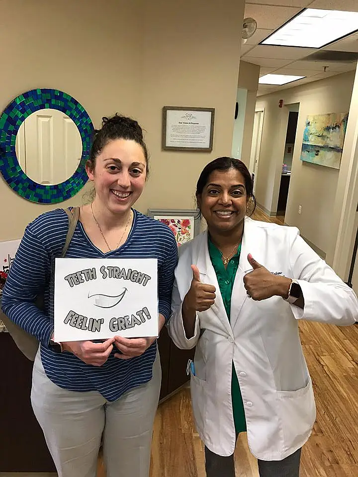 Patient holding a Teeth Straight Feelin' Great sign beside a dentist giving a thumbs up