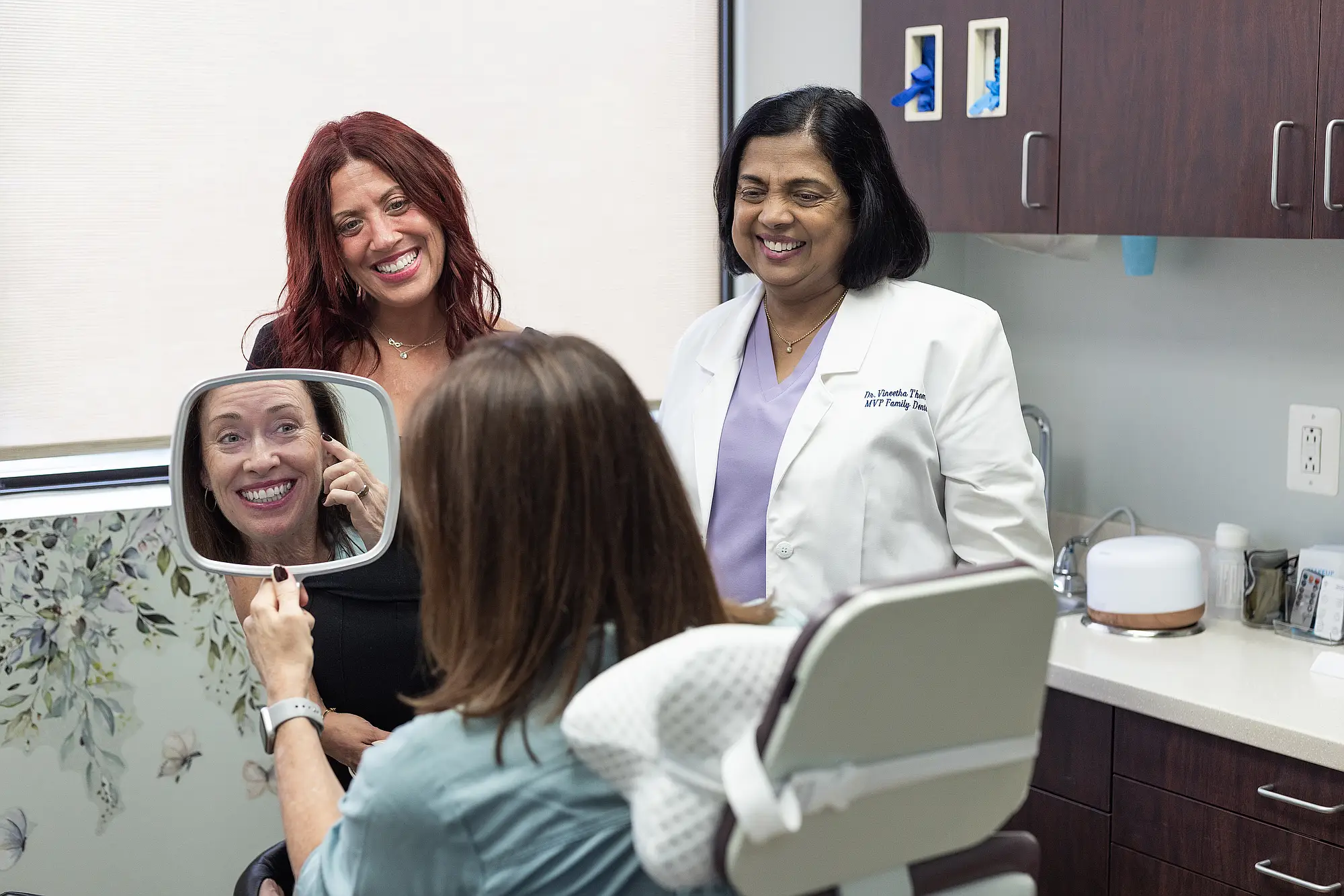 Patient looking at her smile in a mirror with Dr. Vineetha Thomas