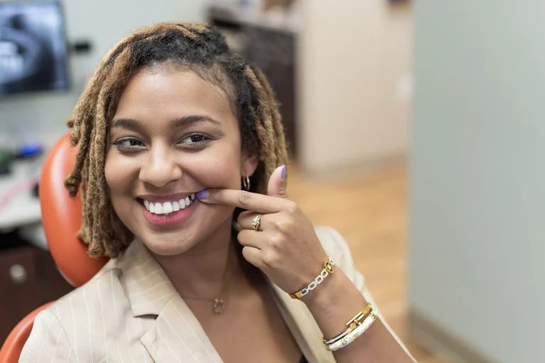 Smiling patient pointing at her teeth in a dental chair